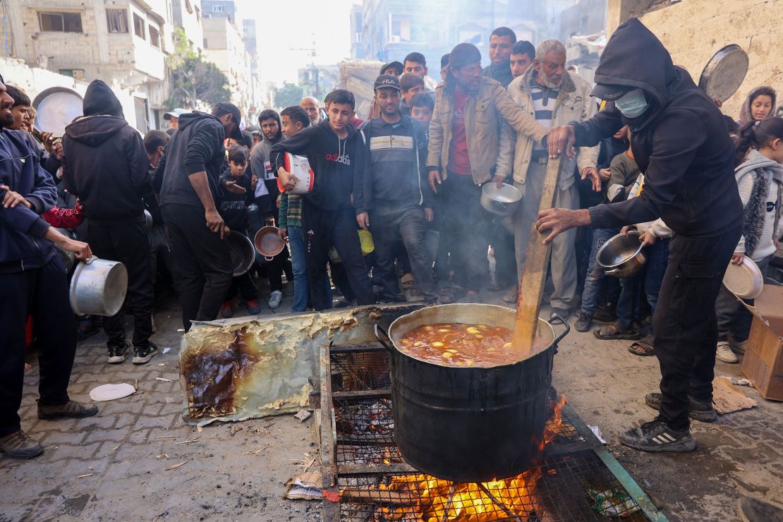 a volunteer stirs a food pot as palestinians wait to collect humanitarian aid portions, in al-shati camp near gaza city on december 26.