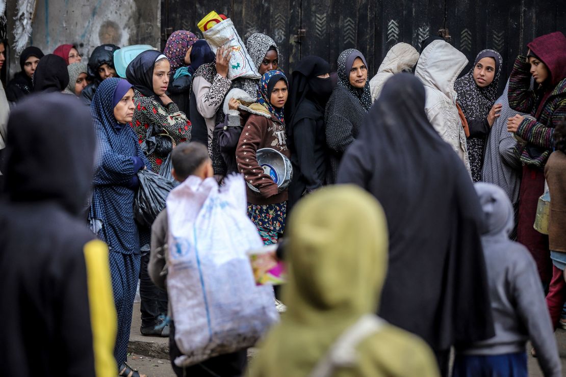 Palestinians lining up with containers to receive free meals in a temporary camp in Deir al-Balah, central Gaza.