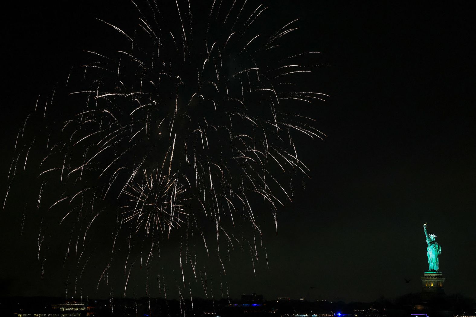 Fireworks explode in the sky above the Statue of Liberty.