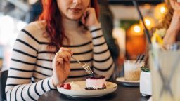 An unrecognizable red-head woman is eating a fruit cake in a coffee shop