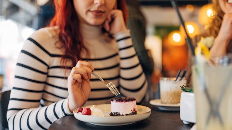 An unrecognizable red-head woman is eating a fruit cake in a coffee shop