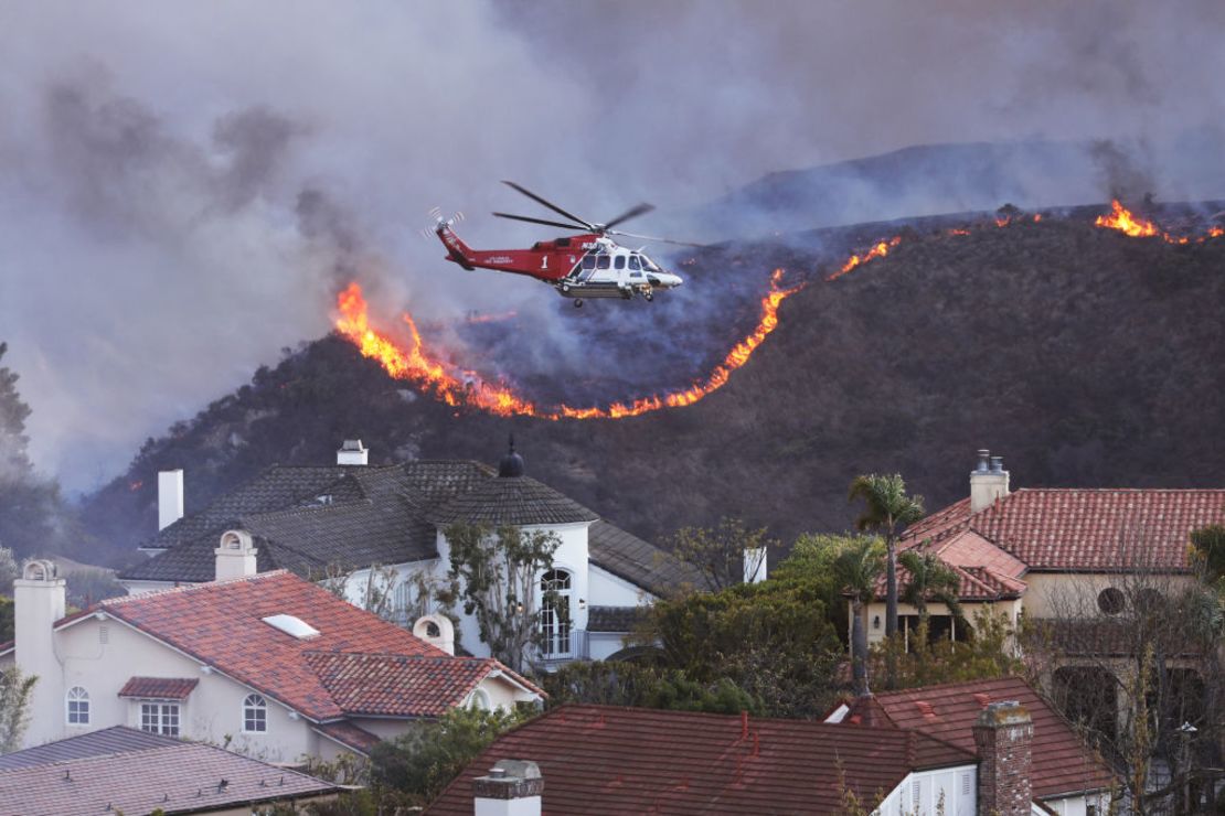 Un helicóptero sobrevuela las casas amenazadas por el incendio de Palisades en Pacific Palisades, California, 7 de enero de 2025. Un rápido incendio forestal en un suburbio de Los Ángeles quemó edificios y provocó evacuaciones el martes debido a los vientos que azotaron la región.