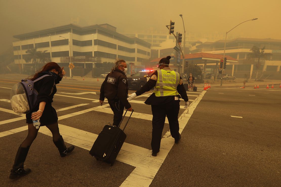 An evacuee is helped across Pacific Coast Highway as smoke from the Palisades Fire envelops Sunset Boulevard on January 7.