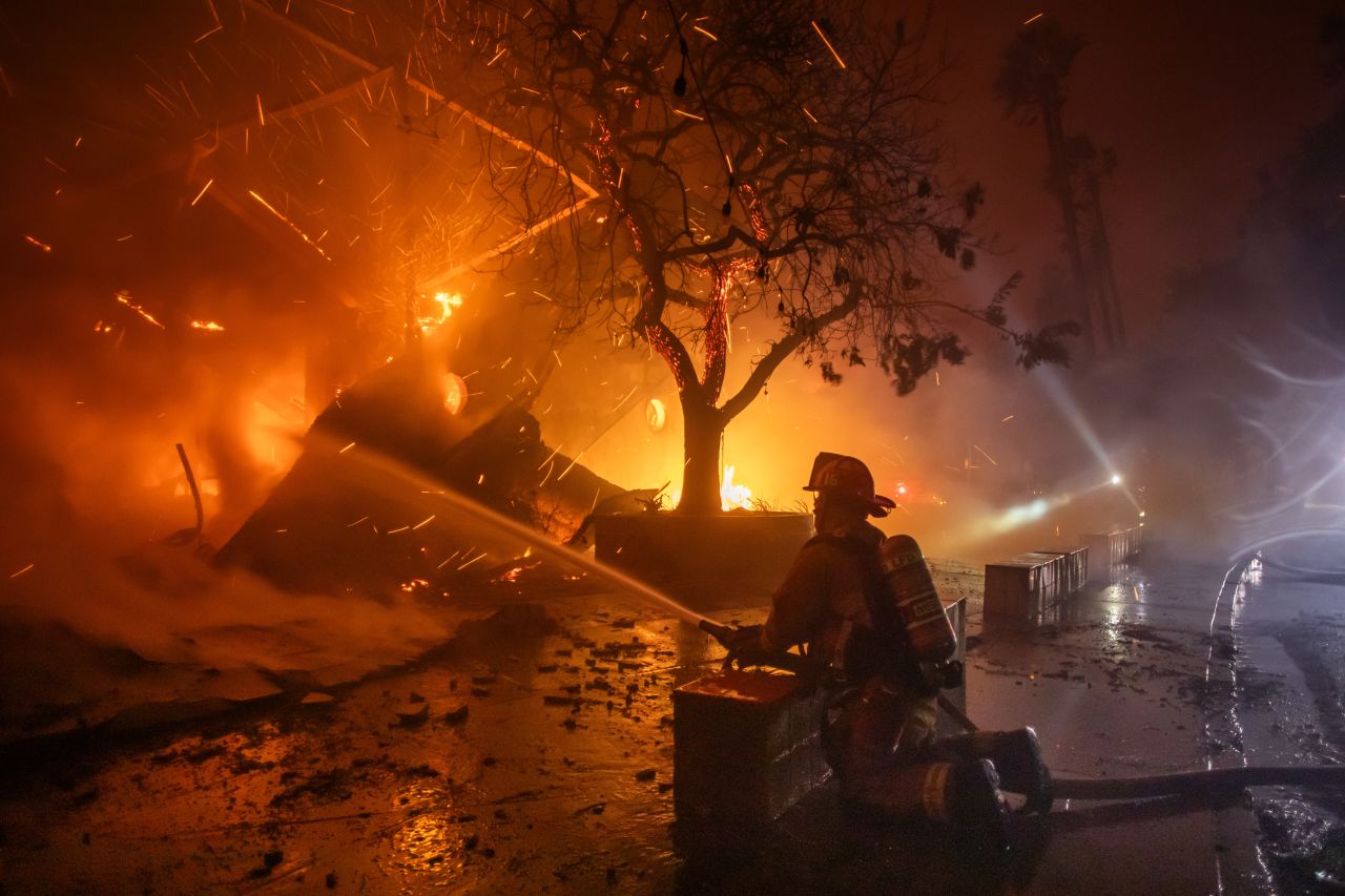 A Firefighter fights the flames from the Palisades Fire burning the Theatre Palisades during a powerful windstorm on January 8, in Los Angeles.