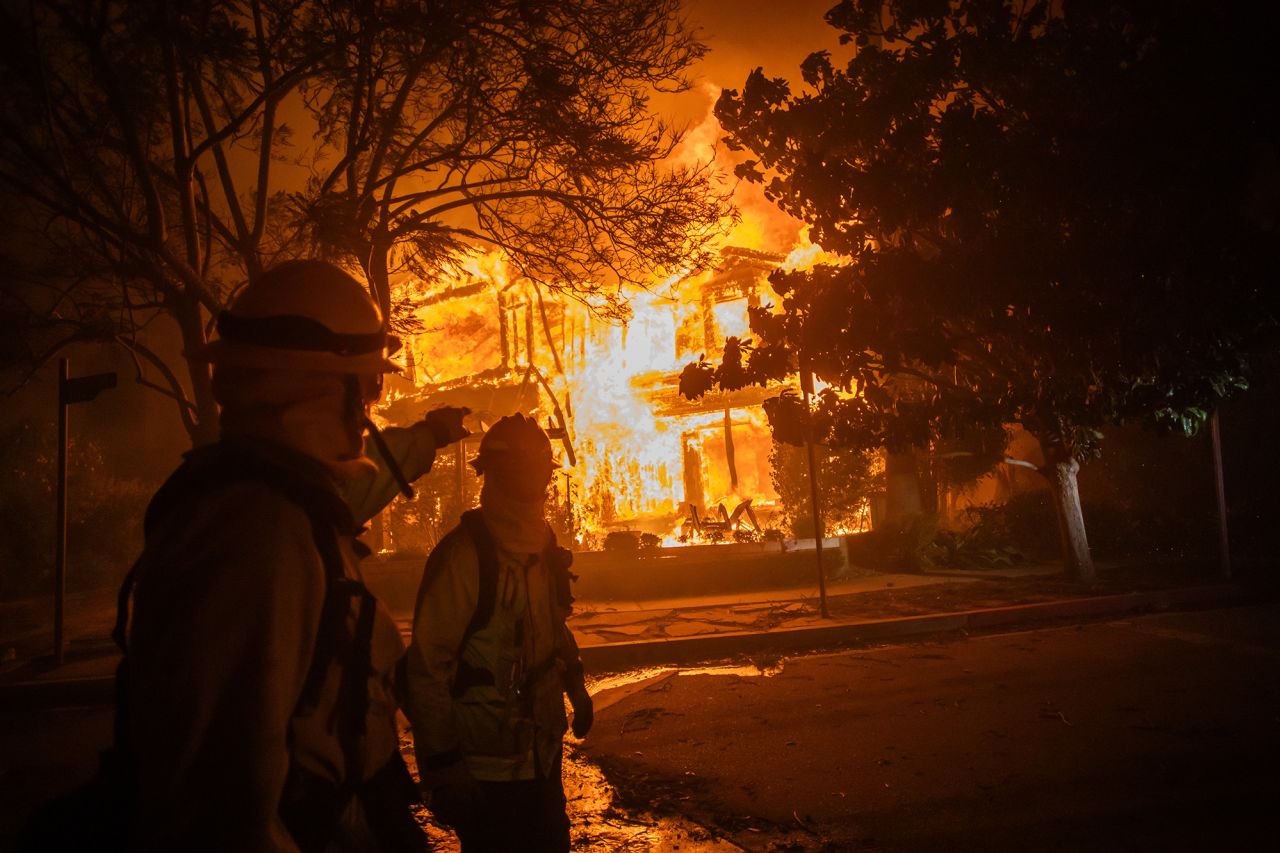 Firefighters walk by a home on flames during a powerful windstorm on January 8, in the Pacific Palisades neighborhood of Los Angeles, California.