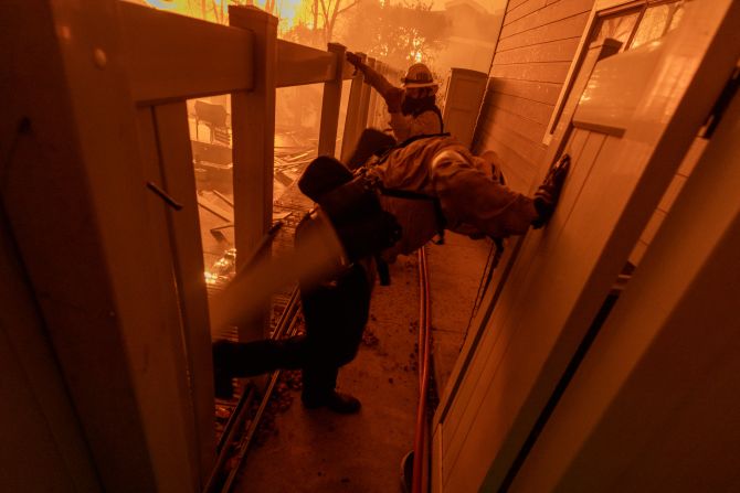 Firefighters kick down a fence as they battle a fire approaching homes in Pasadena.