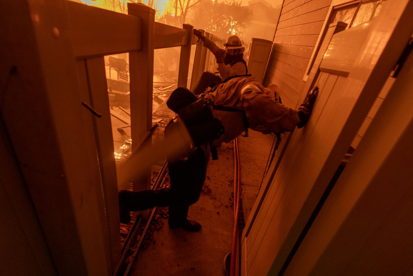 Firefighters kick down a fence Tuesday as they battle a fire approaching homes in Pasadena.