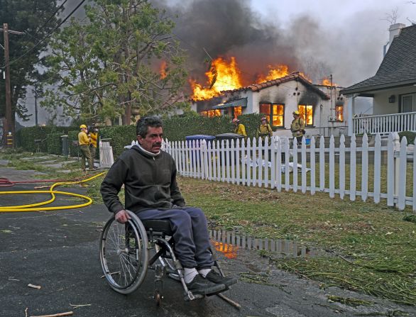 A man wheels past a house on fire in Pasadena.