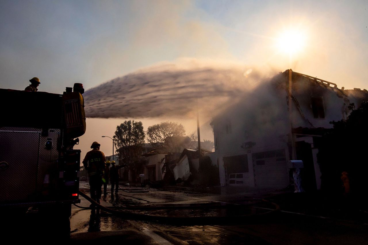 Firefighters hose down a smoldering building on the Pacific Coast Highway during the Palisades fire in Malibu, California,  on Thursday, January 9.