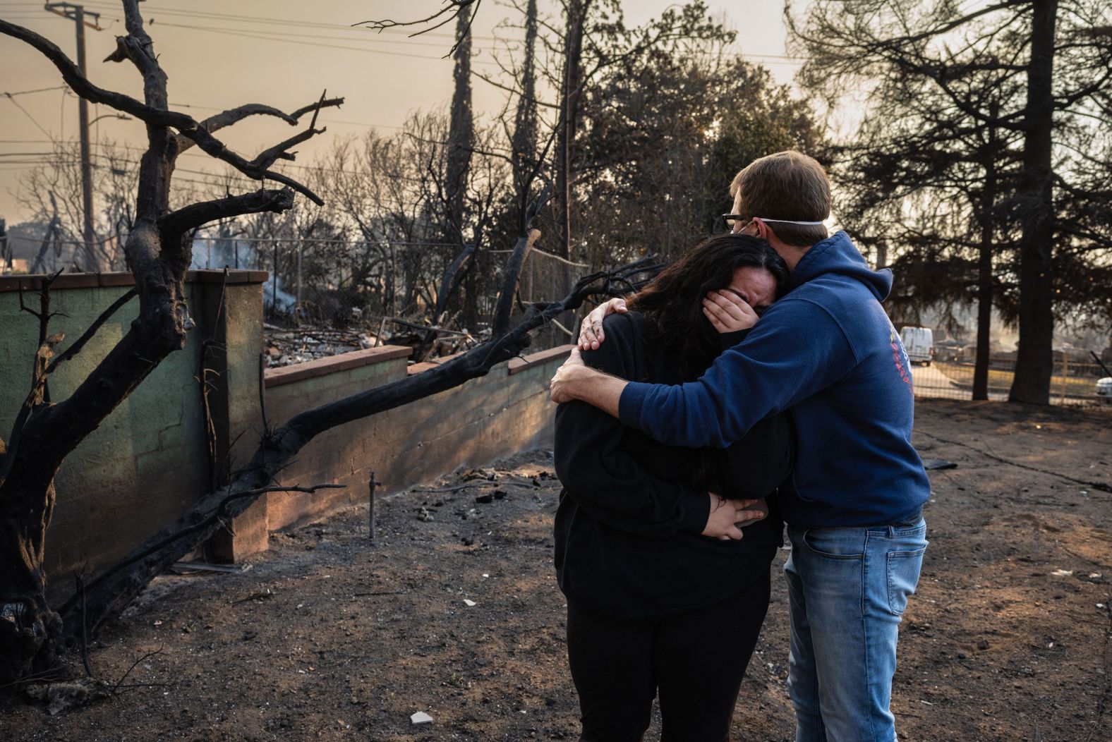 A man comforts his daughter on the charred ruins of their family home in Altadena.