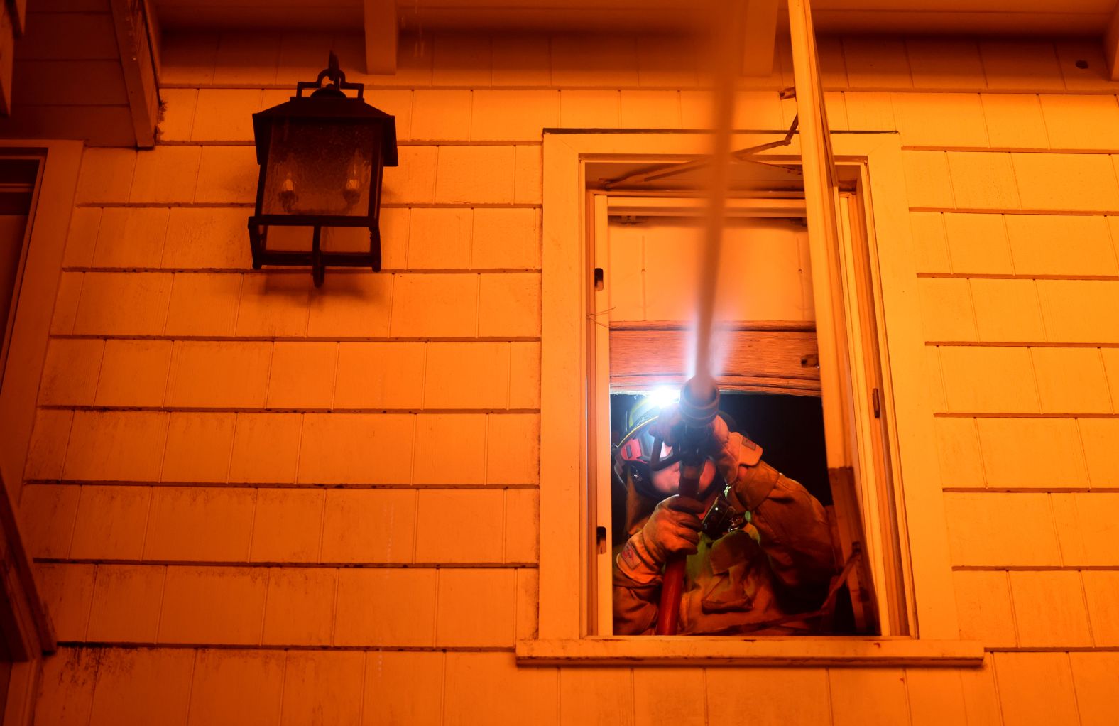 A firefighter battles a house fire from a residence next door as the Palisades Fire burns in Malibu.