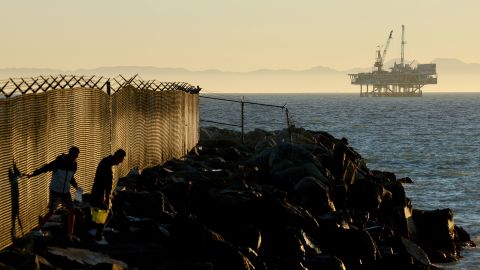 SEAL BEACH, CALIFORNIA - JANUARY 05: People walk along rocks with offshore oil and gas platform Esther in the distance on January 5, 2025 in Seal Beach, California. President Joe Biden will reportedly permanently ban future offshore oil and gas drilling in over 625 million acres of federal waters in an effort to cement his environmental legacy before President-elect Donald Trump is inaugurated January 20th. Platform Esther is located approximately 1.5 miles away from Seal Beach and operates within California state waters. (Photo by Mario Tama/Getty Images)