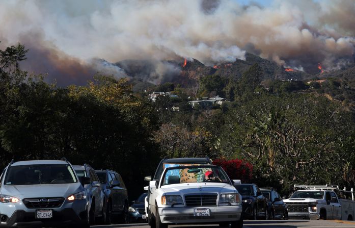 People drive out of harm’s way as the Palisades Fire burns nearby.