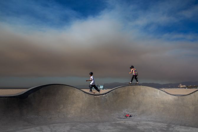 Kids skate at the Venice Skatepark as smoke from the Palisades Fire can be seen in the background.