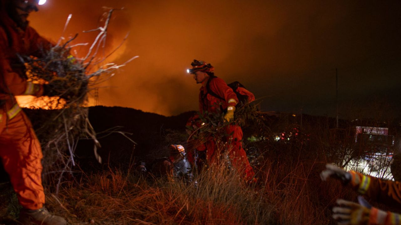 Firefighters work while smoke and flames rise because of the growing Palisades fire in Los Angeles, California, on January 11, 2025. The Palisades Fire, the largest among the Los Angeles wildfires, pushed into new neighborhoods on January 11, prompting additional evacuations and diminishing optimism for containment. Since January 7, several fires have ravaged residential areas across the city, leaving at least 16 people dead and reducing thousands of homes to rubble. US President Joe Biden compared the destruction to a "war zone." (Photo by Peyman Fakhraei / Middle East Images / Middle East Images via AFP) (Photo by PEYMAN FAKHRAEI/Middle East Images/AFP via Getty Images)