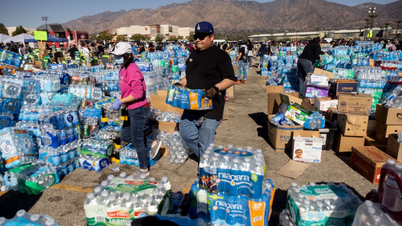 Volunteers carry water for evacuees from the Eaton Fire dwell at a donation center in Santa Anita Park, Arcadia, California, on January 13, 2025. US officials warned "dangerous and strong" winds were set to push deadly wildfires further through Los Angeles residential areas January 12 as firefighters struggled to make progress against the flames. At least 24 people have been confirmed dead from blazes that have ripped through the city, reducing whole neighborhoods to ashes and leaving thousands without homes. (Photo by ETIENNE LAURENT / AFP) (Photo by ETIENNE LAURENT/AFP via Getty Images)