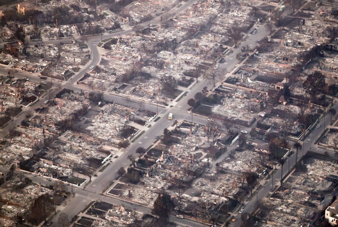 En una vista aérea, un vehículo de emergencia (C) pasa por casas destruidas como el Palisades Fire sigue ardiendo el 09 de enero 2025 en Pacific Palisades, California. Múltiples incendios forestales alimentados por los intensos vientos de Santa Ana están ardiendo en todo el condado de Los Ángeles.