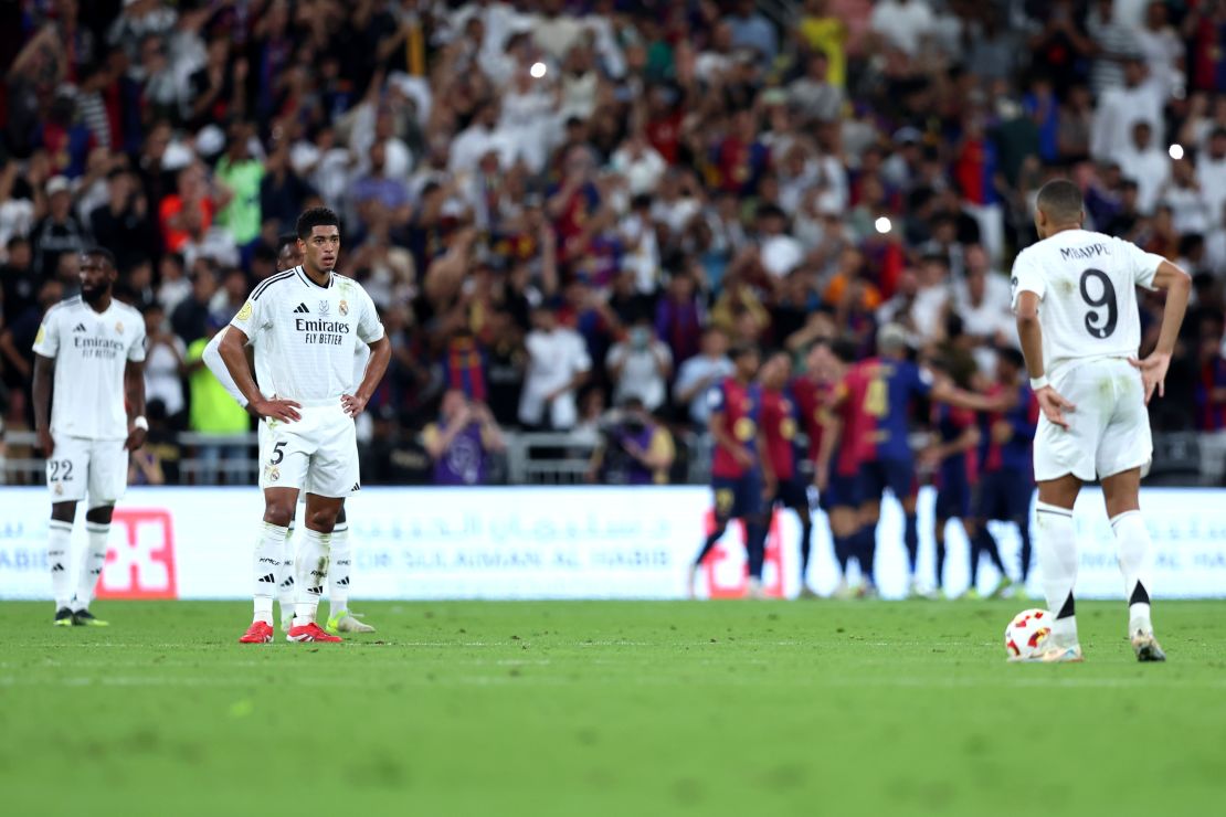 Jude Bellingham, del Real Madrid, mira a su compañero Kylian Mbappé mientras Raphinha, del FC Barcelona (en la oscuridad), celebra el tercer gol de su equipo durante la final de la Supercopa de España entre el Real Madrid y el FC Barcelona en la Ciudad Deportiva Rey Abdullah el 12 de enero de 2025 en Yeda, Arabia Saudita.