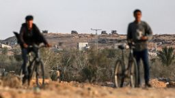 Vehículos militares israelíes se desplegaron detrás de dos jóvenes con bicicletas en una carretera al este de Deir el-Balah, en el centro de Gaza, el domingo, después de que se alcanzara un acuerdo de alto el fuego.