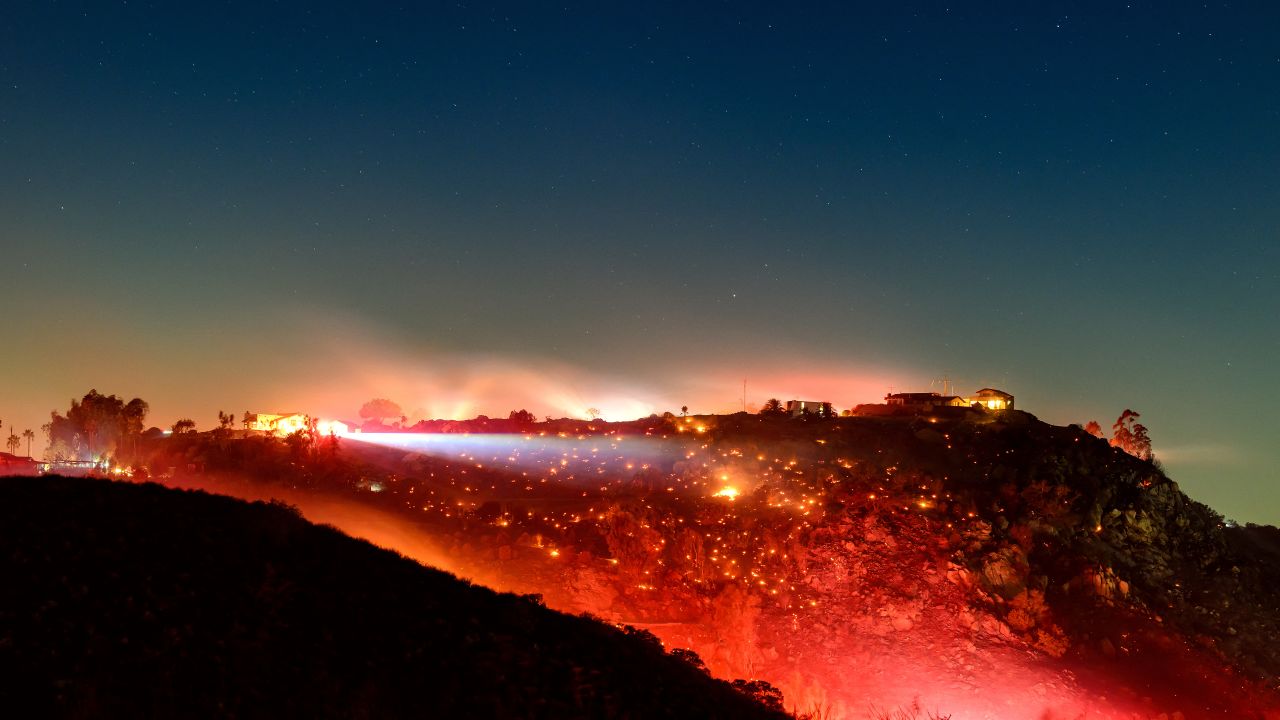 In this long exposure photo, fire smolders on a hillside during the Lilac fire in unincorporated San Diego County, California on January 21, 2025. Exhausted Los Angeles firefighters on January 20 braced for the return of yet more dangerously strong gusts, as California's governor slammed "hurricane-force winds of misinformation" surrounding blazes that have killed 27 people. The two largest fires, which have obliterated almost 40,000 acres (16,000 hectares) and razed entire neighborhoods of the second biggest US city, were both now more than half contained, officials announced. (Photo by JOSH EDELSON / AFP) (Photo by JOSH EDELSON/AFP via Getty Images)