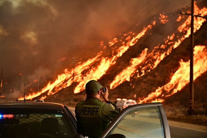 A law enforcement officer takes photos as flames from the Hughes Fire race up a hill in Castaic.