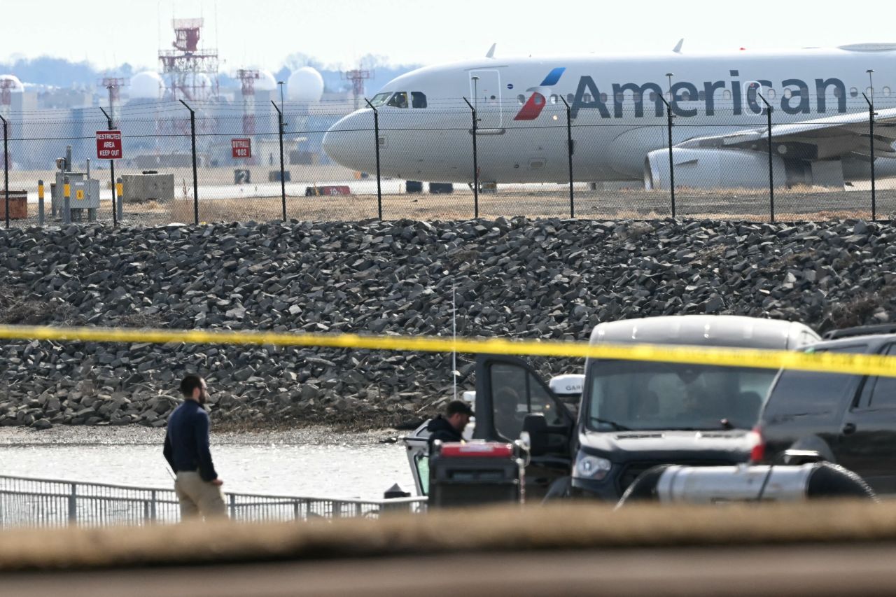 An American Airlines plane prepares to take off as investigators carry pieces of wreckage from the waters of the Potomac River after American Airlines flight 5342 on approach to Reagan National Airport crashed into the river after colliding with a US Army helicopter, near Washington, DC, on January 30, 2025. There are likely no survivors from a collision between a passenger jet and US Army helicopter in Washington, officials said Thursday, as recovery operations pulled 28 bodies from the river into which both crashed. (Photo by ANDREW CABALLERO-REYNOLDS / AFP) (Photo by ANDREW CABALLERO-REYNOLDS/AFP via Getty Images)