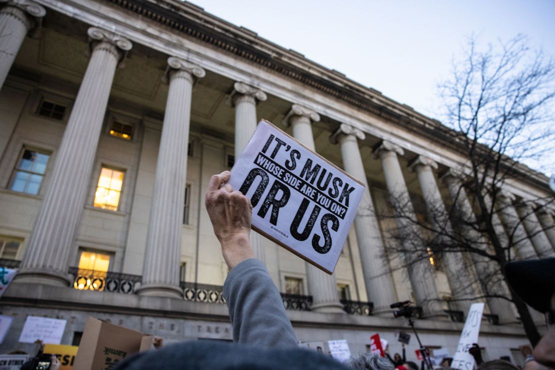 Um manifestante mantém uma placa durante um comício em protesto contra Elon Musk e o Departamento de Eficiência do Governo, em frente ao Departamento do Tesouro dos EUA em 4 de fevereiro de 2025.