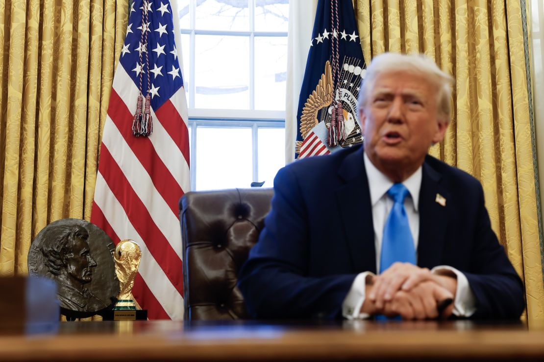 A replica FIFA World Cup trophy can be seen behind President Donald Trump when he speaks with reporters in the Oval Office.