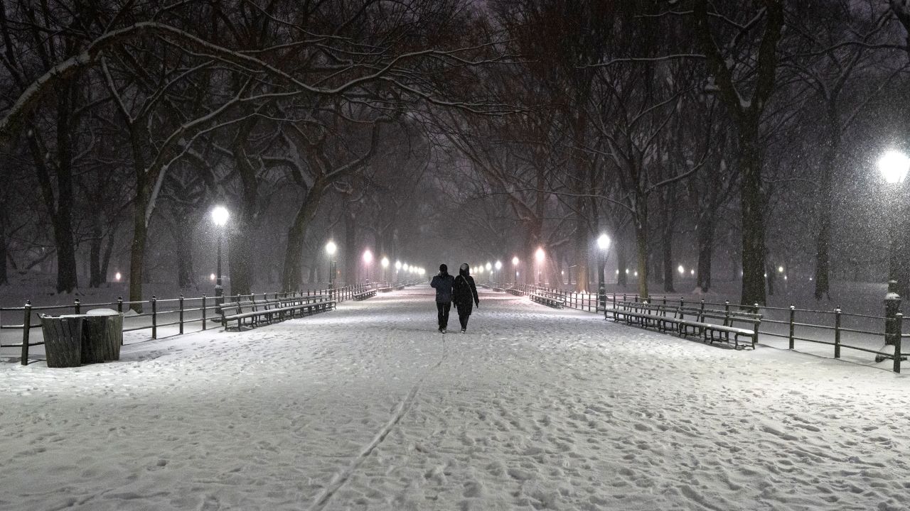 People walk through The Mall as snow falls in Central Park at night on February 08, 2025 in New York City.
