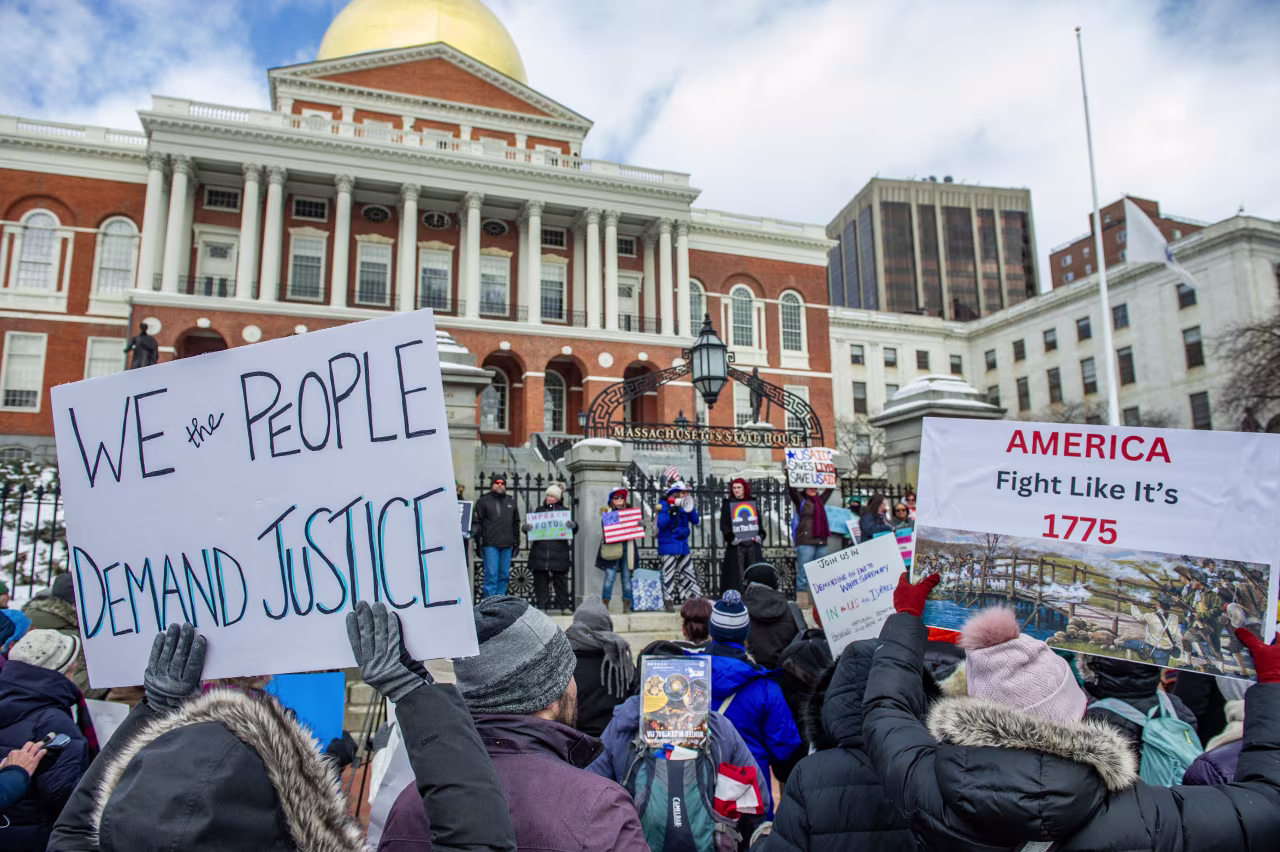 Demonstrators hold signs as they rally against US President Donald Trump and his policies during a protest outside the Massachusetts Statehouse on Presidents' Day on Monday, in Boston, Massachusetts.