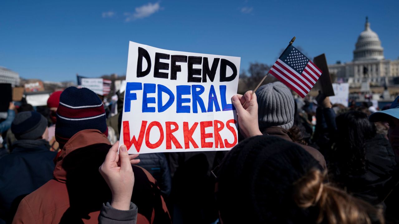 A demonstrator holds a sign in support of federal workers during a President's Day protest near the US Capitol in Washington, DC, US, on Monday, Feb. 17, 2025. Thousands of probationary employees in multiple government agencies are facing dismissal as the Trump administration continued its effort to rapidly thin the ranks of federal workers. Photographer: Stefani Reynolds/Bloomberg via Getty Images