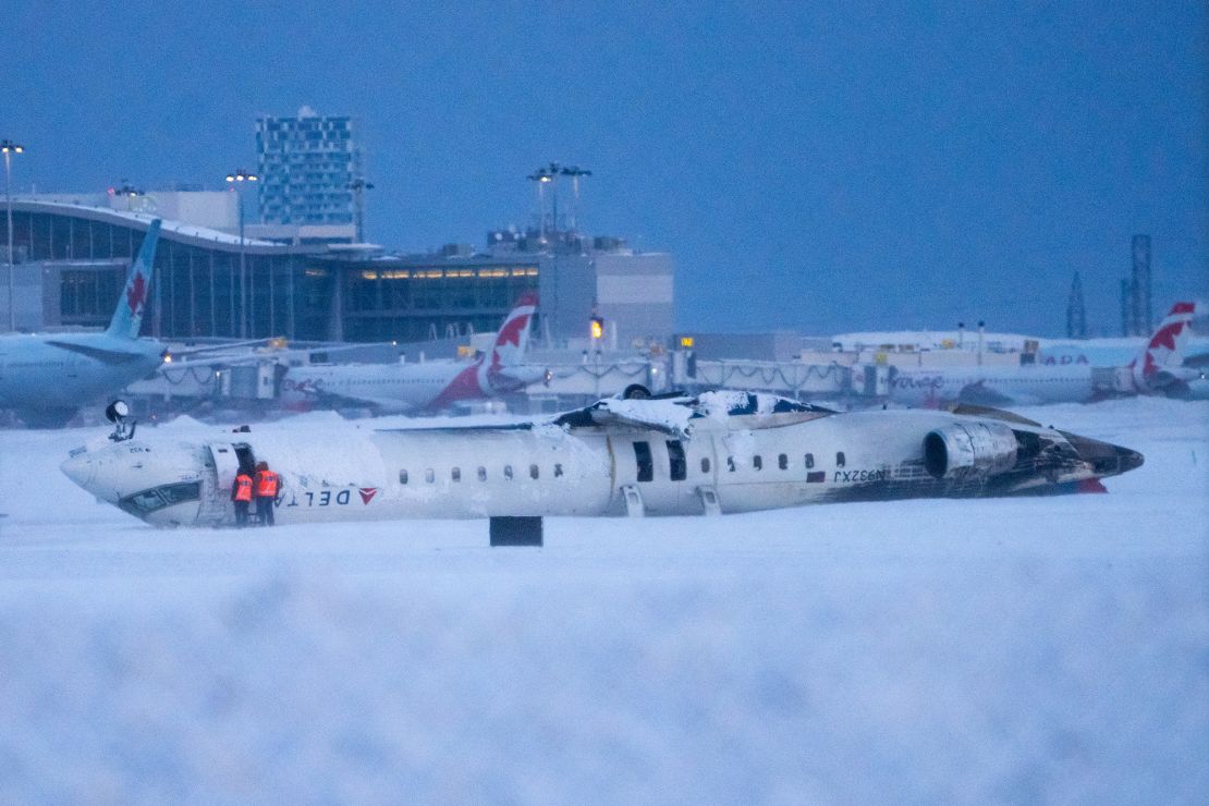 Airport workers survey the site of a Delta Air Lines plane crash that injured at least 18 passengers at Toronto Pearson International Airport on February 18. No one was killed in the crash.