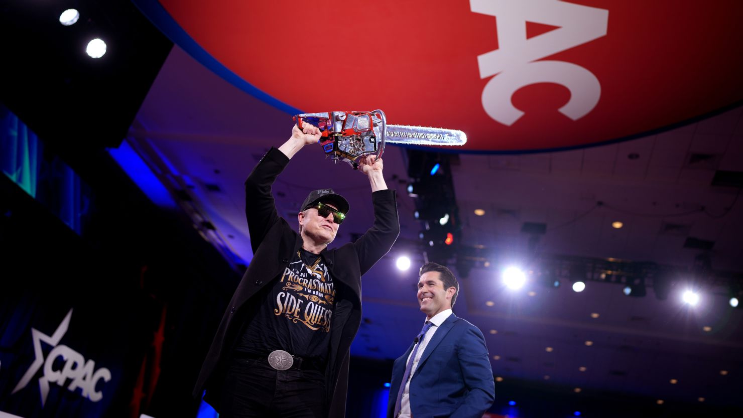 Tesla CEO Elon Musk wields a chainsaw next to Newsmax anchor Rob Schmitt at the Conservative Political Action Conference on February 20, 2025, in Oxon Hill, Maryland.