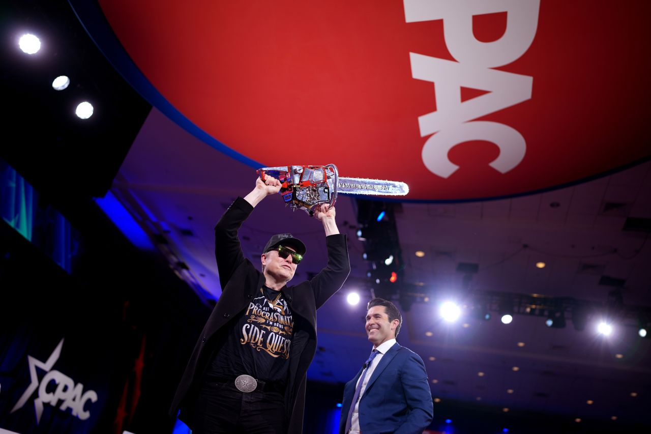 Elon Musk wields a chainsaw as he leaves the stage alongside Newsmax anchor Rob Schmitt in Oxon Hill, Maryland, on Thursday.