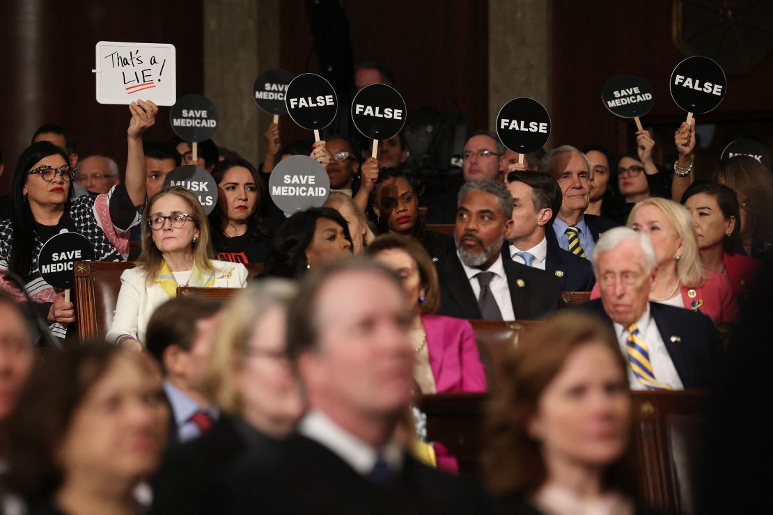 Democrats hold protest signs as President Donald Trump speaks.