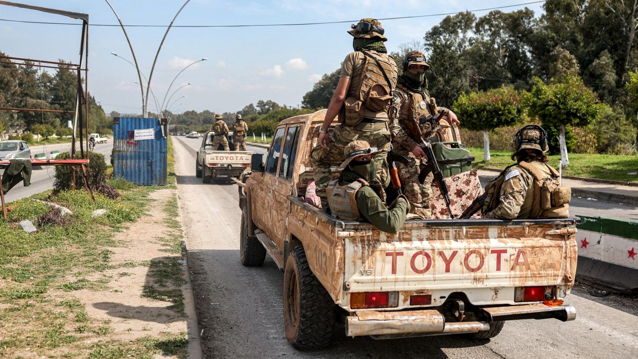 Security forces loyal to the interim Syrian government ride in the back of a vehicle moving along a road in Syria's western city of Latakia on March 9, 2025. Syria's interim President Ahmed al-Sharaa called for national unity and peace on March 9, amid growing international backlash following the killing of civilians along the country's coast in the worst violence since the overthrow of former president Bashar al-Assad, in the heartland of the Alawite minority to which the latter belongs.