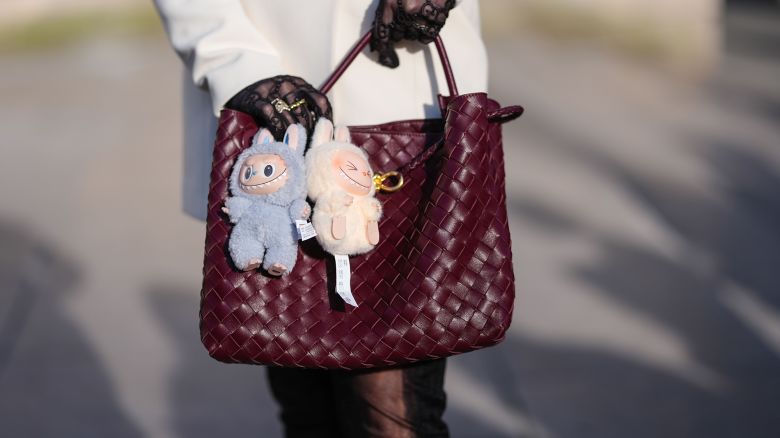 A guest wears a burgundy bordeaux woven Bottega Veneta Andiamo leather bag, light blue Labubu bag charm, cream Labubu bag charm, outside Elie Saab, during the Paris Fashion week Women's Fall/Winter 2025-2026 on March 8, 2025 in Paris, France.