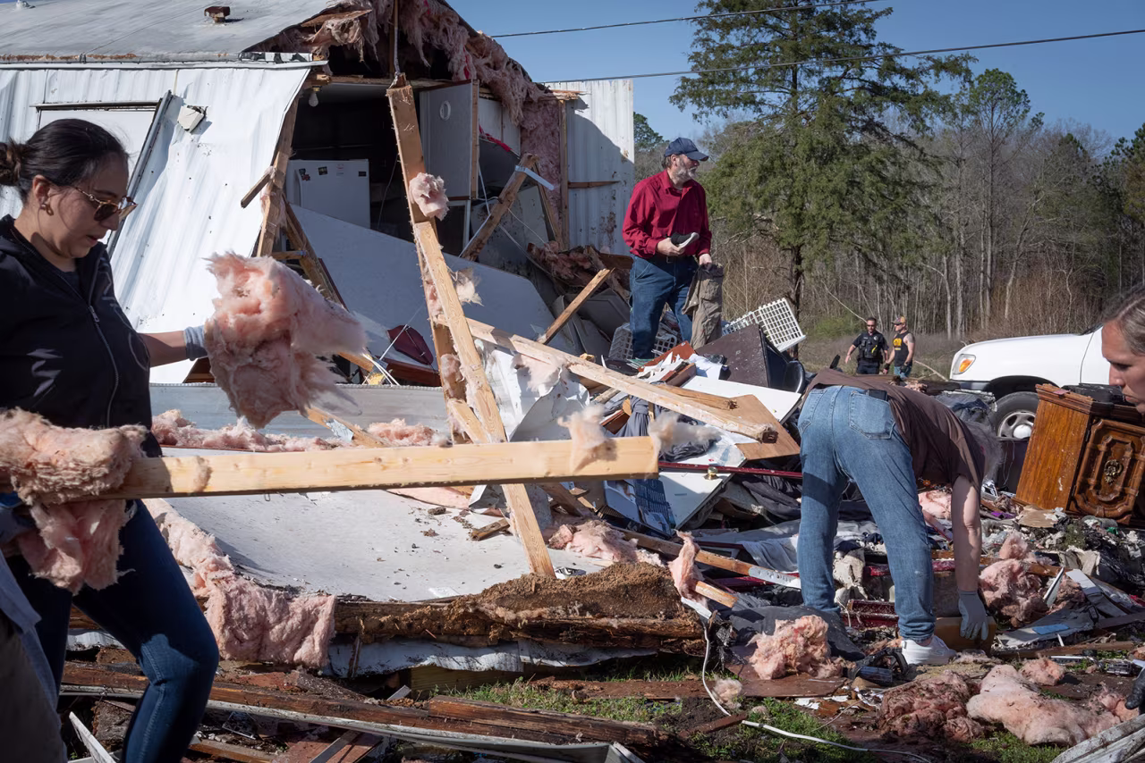 Tim Striegel, in red shirt goes though his damaged belongings while volunteers help him clean up after his mobile home was hit by a tornado in Calera, Alabama on Sunday.