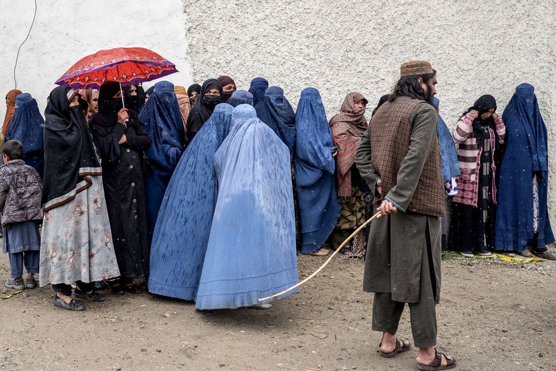 A Taliban guard keeps watch as women wait in line in Kabul in the midst of a downpour to receive food supplies donated during the Muslim holy month of Ramadan, on March 25, 2025.