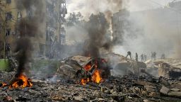 A firefighter sprays water on the debris as people gather at the site of an Israeli strike in southern Beirut on Friday.
