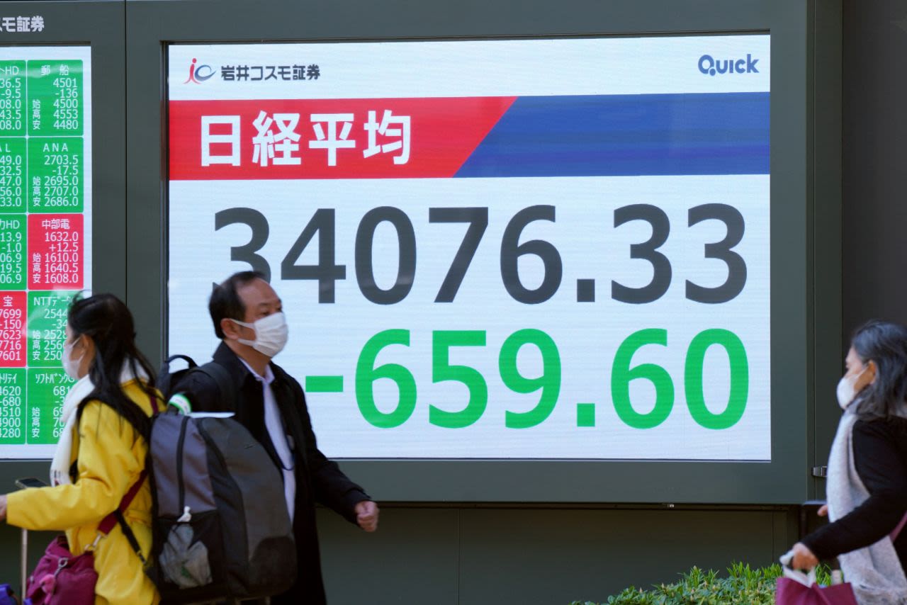 Personas caminan junto a un tablero electrónico que muestra las cifras del Nikkei Stock Average en la bolsa de Tokio, en una calle de Tokio el viernes.