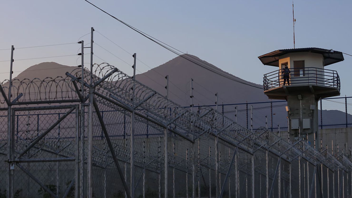 Un oficial de prisiones vigila desde la torre de observación con el volcán San Vicente al fondo en el centro penitenciario de máxima seguridad CECOT (Centro de Alojamiento Obligatorio de Terrorismo) el 4 de abril de 2025 en Tecoluca, San Vicente, El Salvador.