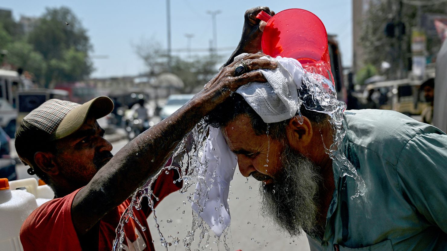 A volunteer pours water on a pedestrian's head to cool off during a hot summer day along a street in Karachi on April 5, 2025.
