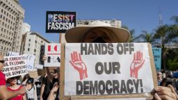 A woman holds a sign reading "Hands Off Our Democracy" at a crowded rally in Los Angeles on April 5, 2025. The protest is part of a global "Hands Off!" action organized across all 50 US states and internationally, opposing what activists describe as a hostile takeover of American democracy by Donald Trump and Elon Musk. (Photo by Ali Matin / Middle East Images / Middle East Images via AFP) (Photo by ALI MATIN/Middle East Images/AFP via Getty Images)          