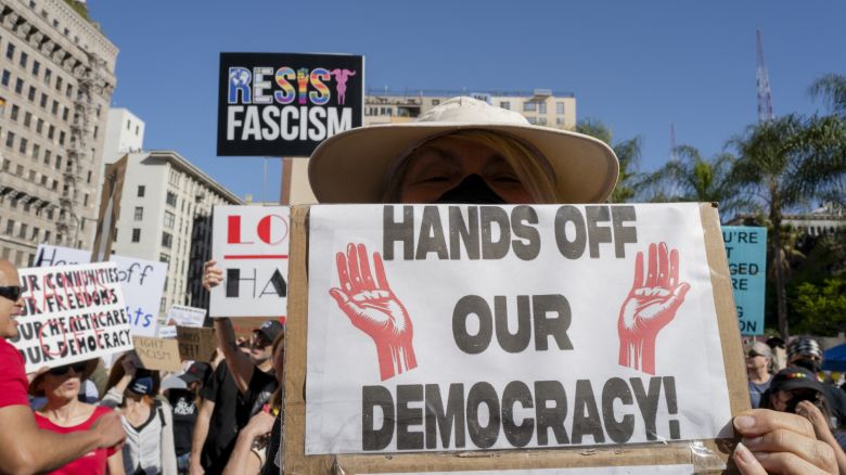 A woman holds a sign reading "Hands Off Our Democracy" at a crowded rally in Los Angeles on April 5, 2025. The protest is part of a global "Hands Off!" action organized across all 50 US states and internationally, opposing what activists describe as a hostile takeover of American democracy by Donald Trump and Elon Musk. (Photo by Ali Matin / Middle East Images / Middle East Images via AFP) (Photo by ALI MATIN/Middle East Images/AFP via Getty Images)          