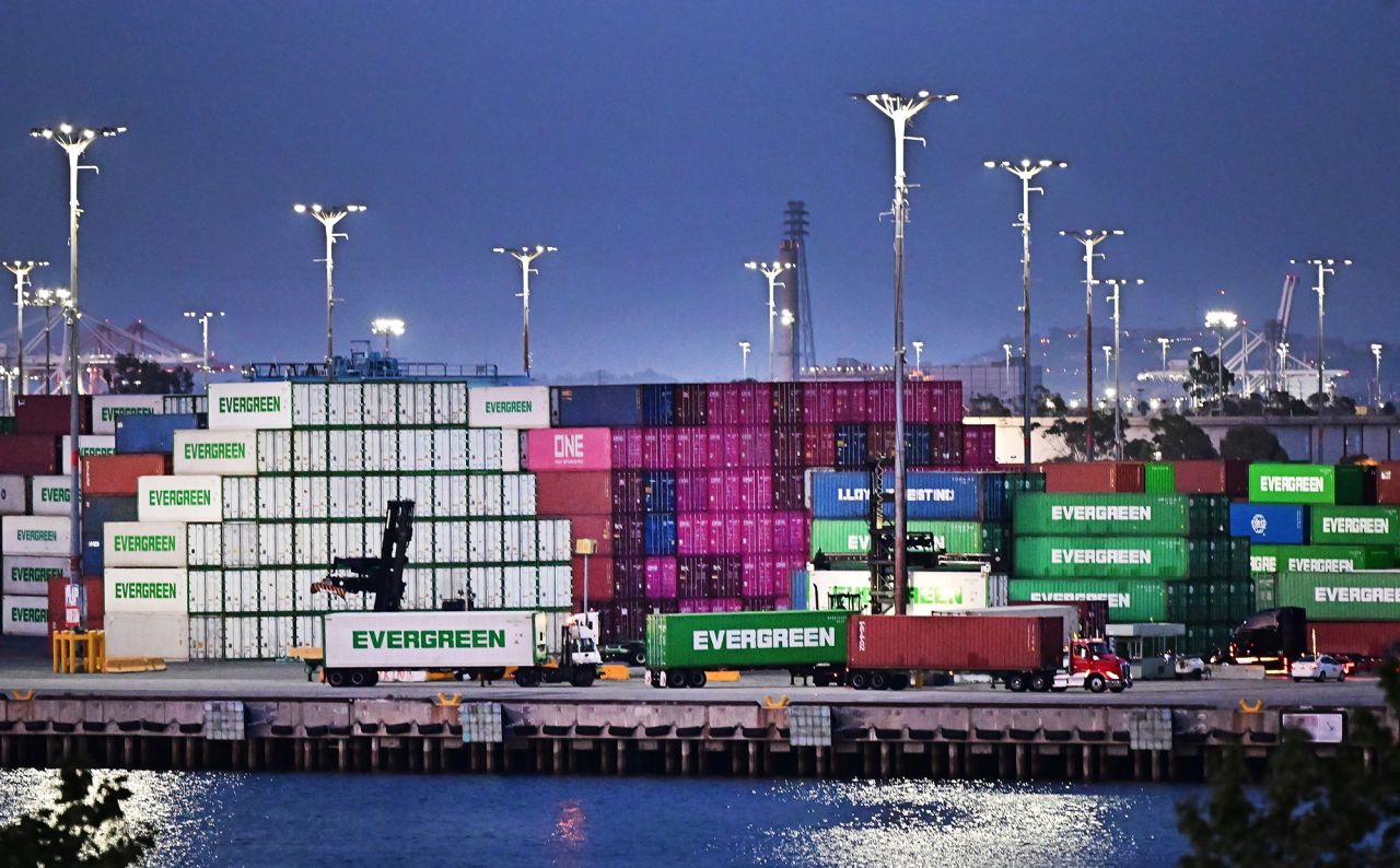 The container trucks head in front of the shipping containers stacked at the port of Los Angeles on April 14.