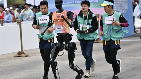 A robot and its engineers run in the humanoid robot half marathon in Beijing on April 19, 2025. Dozens of humanoid robots took to the streets of Beijing, ing thousands of their flesh-and-blood counterparts in a world-first half marathon showcasing China's drive to lead the global race in cutting-edge technology. (Photo by Pedro PARDO / AFP) (Photo by PEDRO PARDO/AFP via Getty Images)          