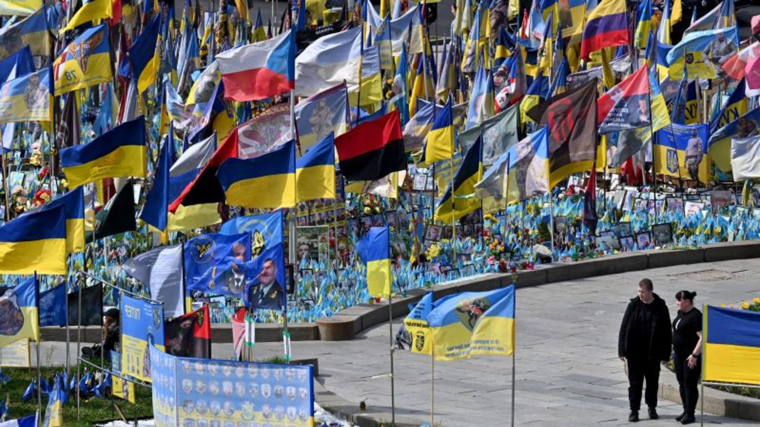 Una pareja camina entre banderas y retratos de militares caídos en un monumento improvisado para los combatientes ucranianos y extranjeros caídos, en la Plaza de la Independencia de Kyiv, Ucrania, el sábado.