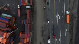 In an aerial view, trucks carrying shipping containers drive through the Port of Oakland.