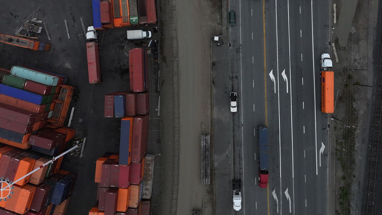 In an aerial view, trucks carrying shipping containers drive through the Port of Oakland.